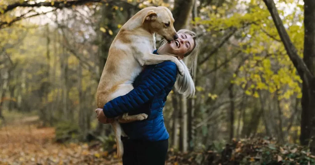 Frau trägt Hund auf dem Arm und lacht